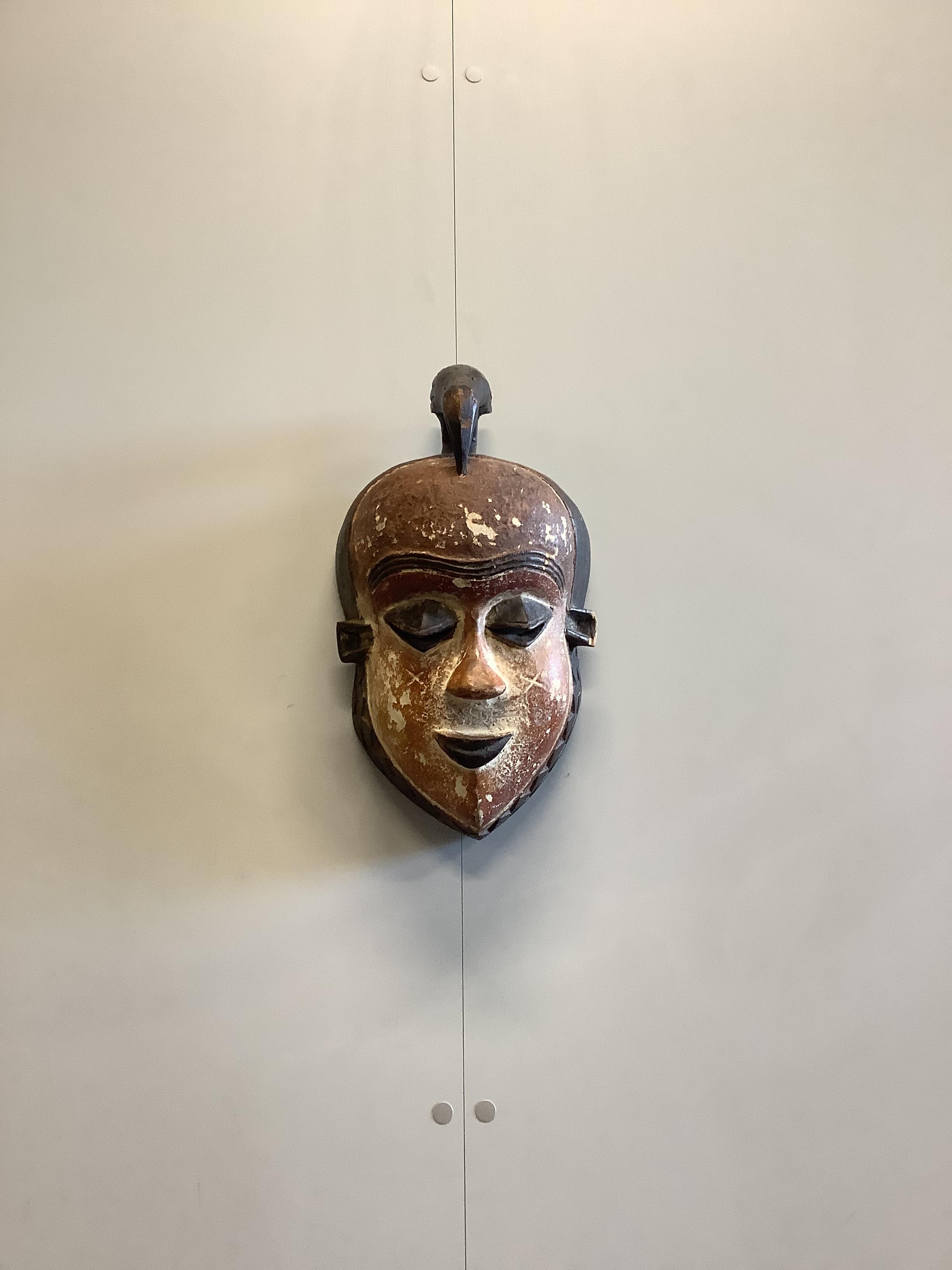 An African Ashanti hardwood stool, width 54cm, depth 33cm, height 35cm together with a painted carved hardwood face mask